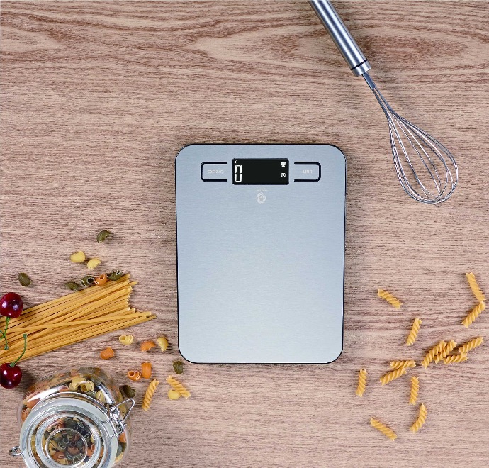 alt="electric scale placed on wooden table next to pasta and whisker"